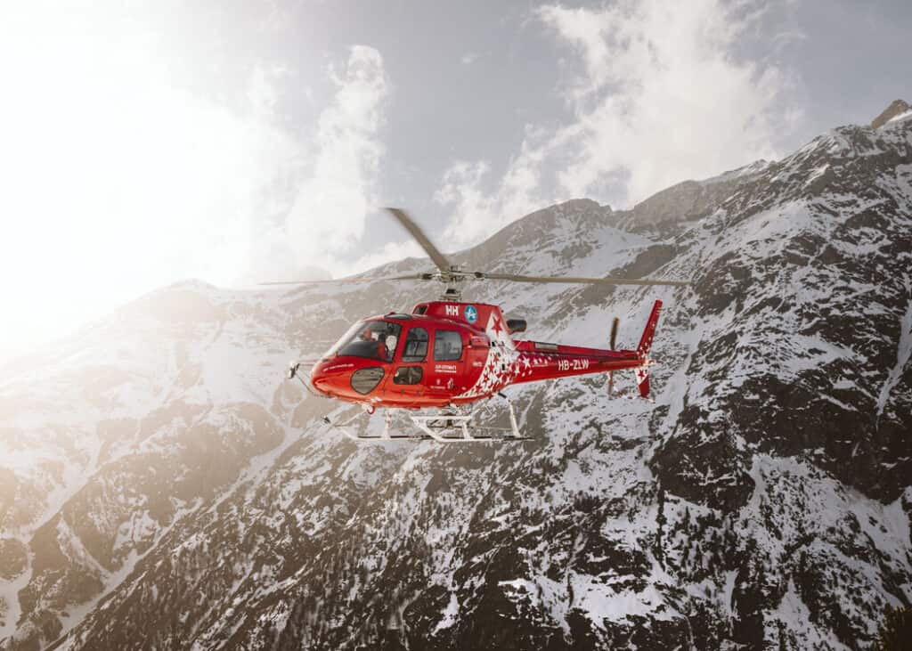 Jasper-Helicopter-Tours-red-heli-flying-with-mountain-range-as-backdrop